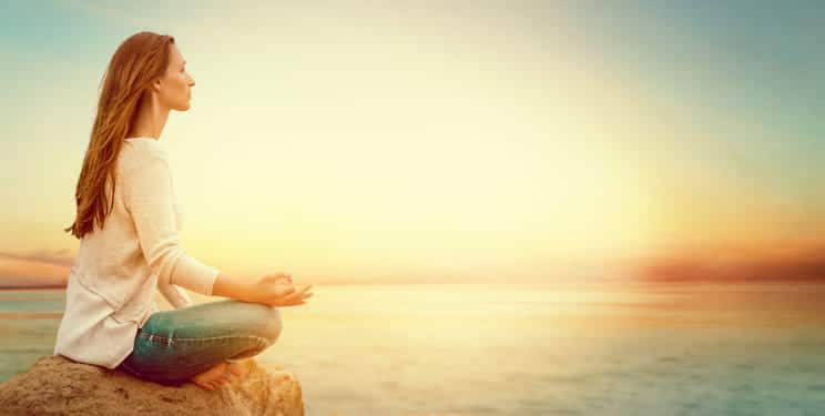 Dieses Bild zeigt eine Frau am Strand, die meditiert.